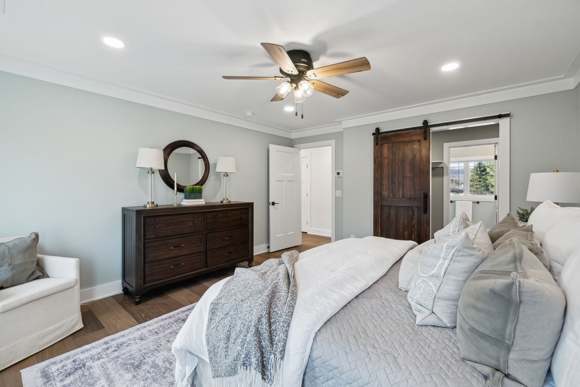 Bedroom with wood floors, light blue walls, a dark wooden dresser, and a rustic sliding door.
