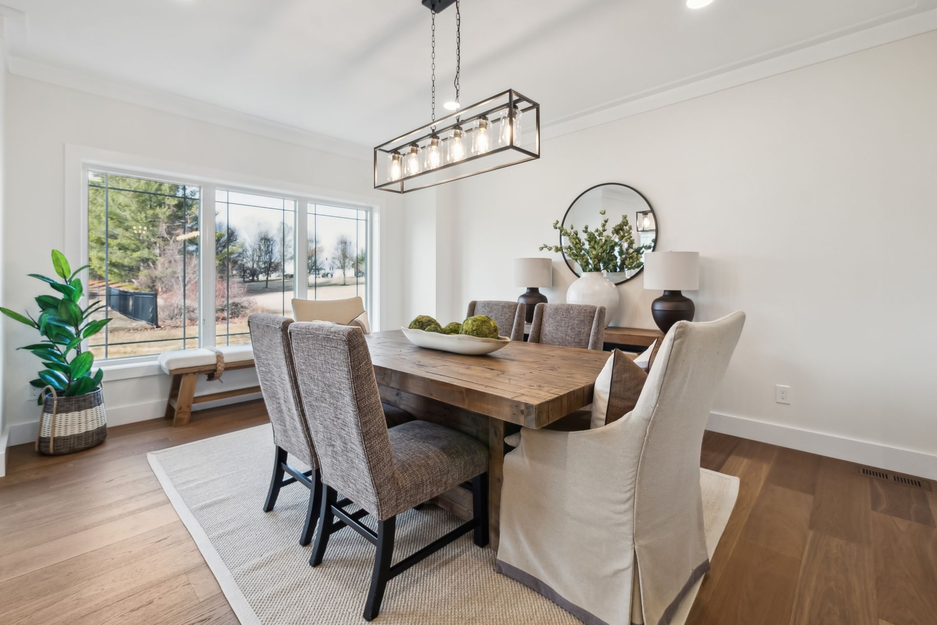 Formal dining room with wooden table, six upholstered chairs, rug, window, and decorative lighting.