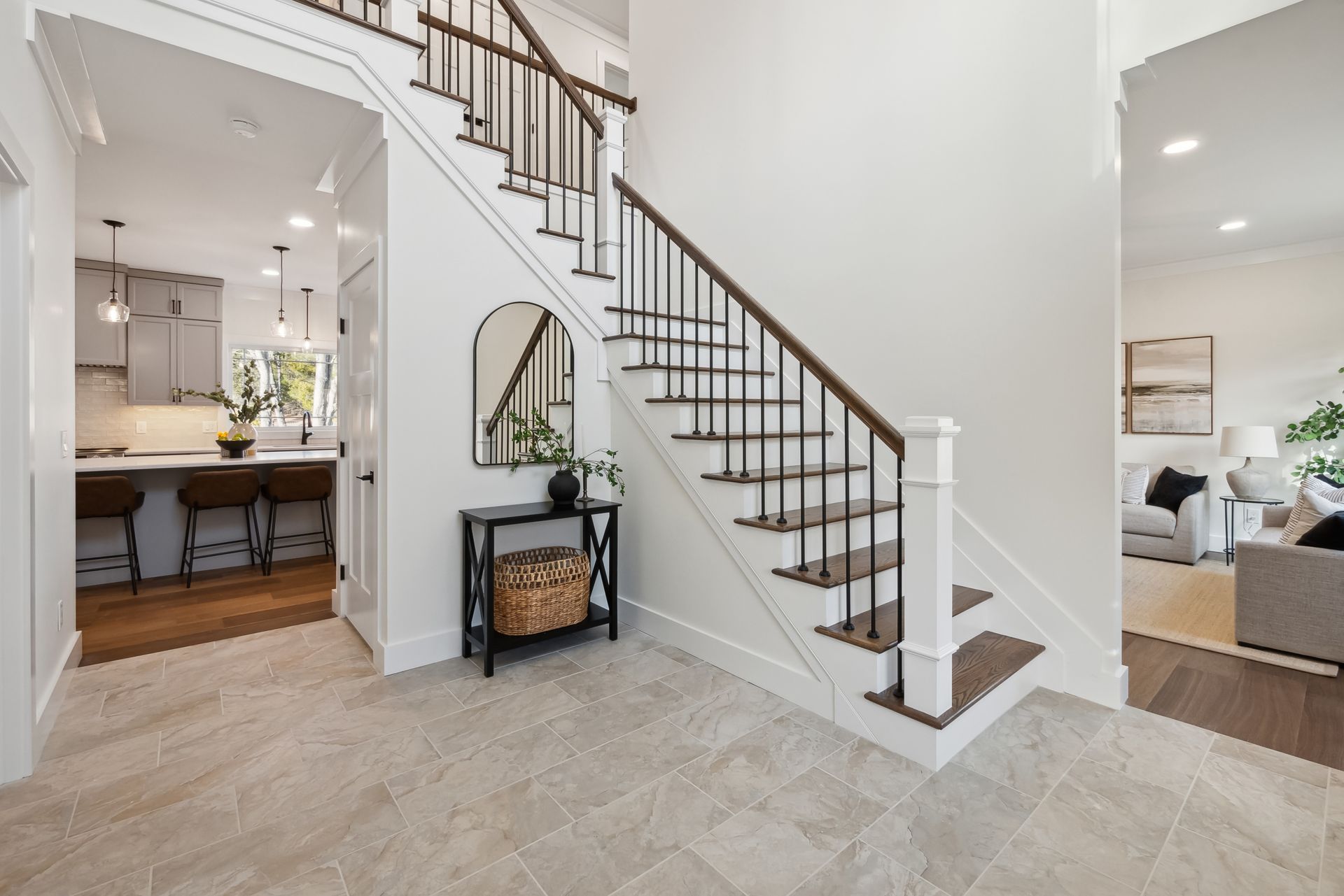 Entryway with staircase and view into kitchen, neutral color scheme, black accents.