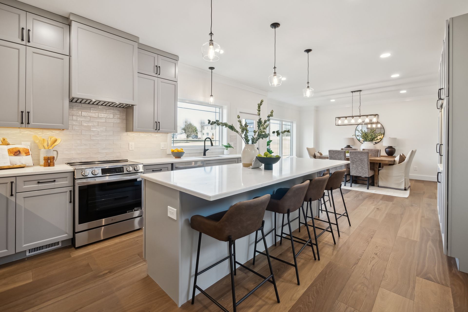 Modern kitchen with gray cabinets, island with bar stools, and dining area.