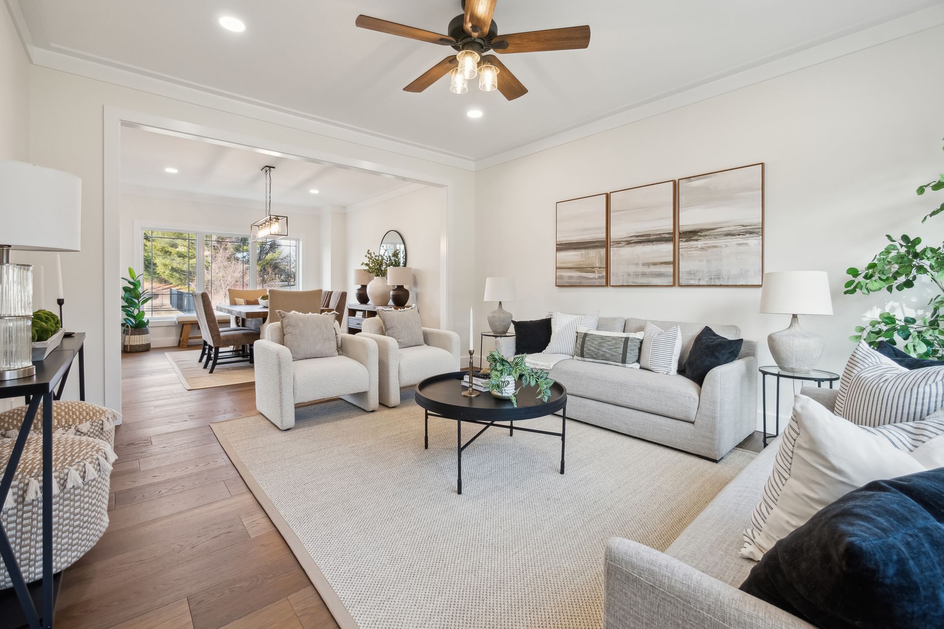 Living room with white walls, sofa, chairs, rug, and a view into the dining area.