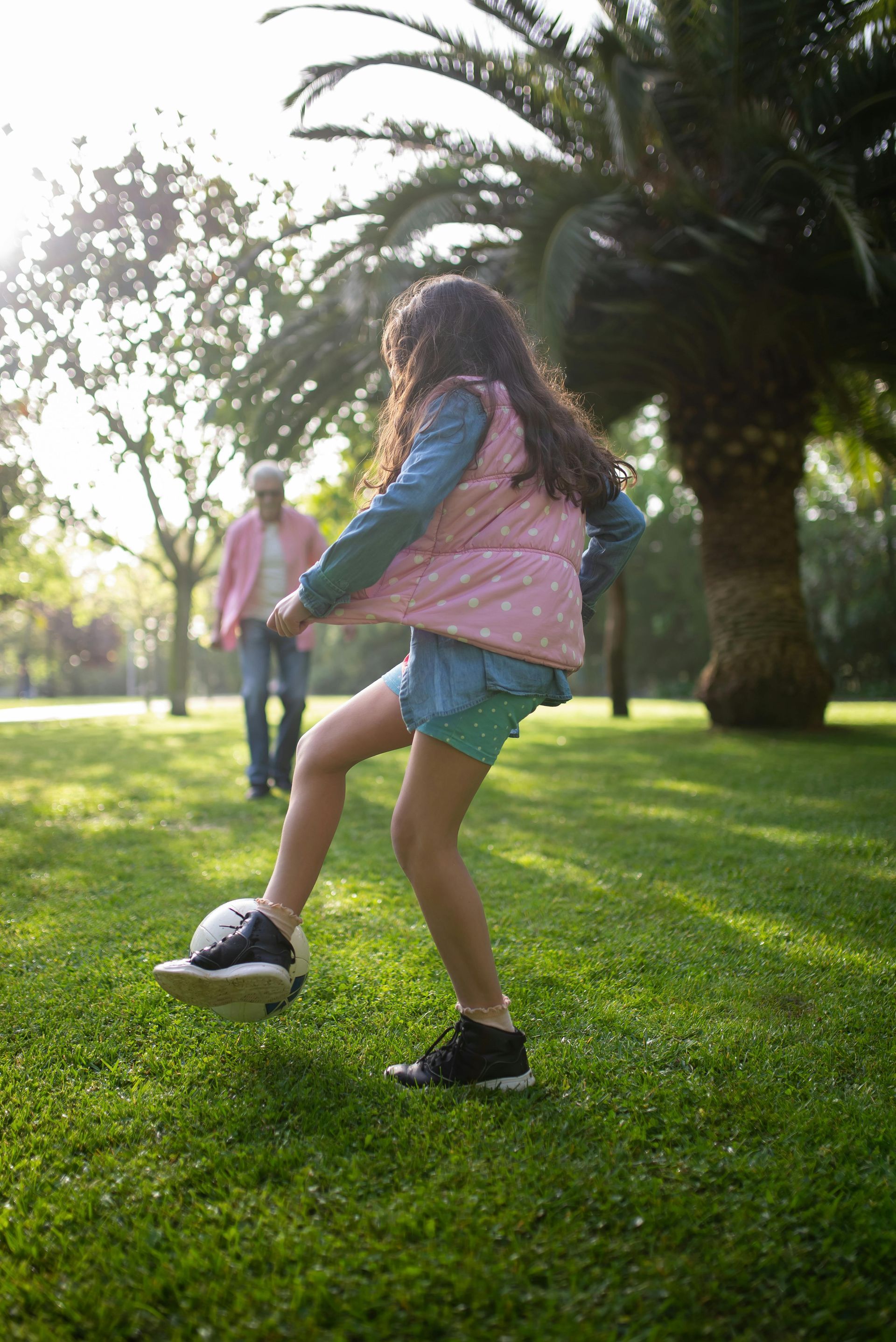 A little girl is kicking a soccer ball in a park.