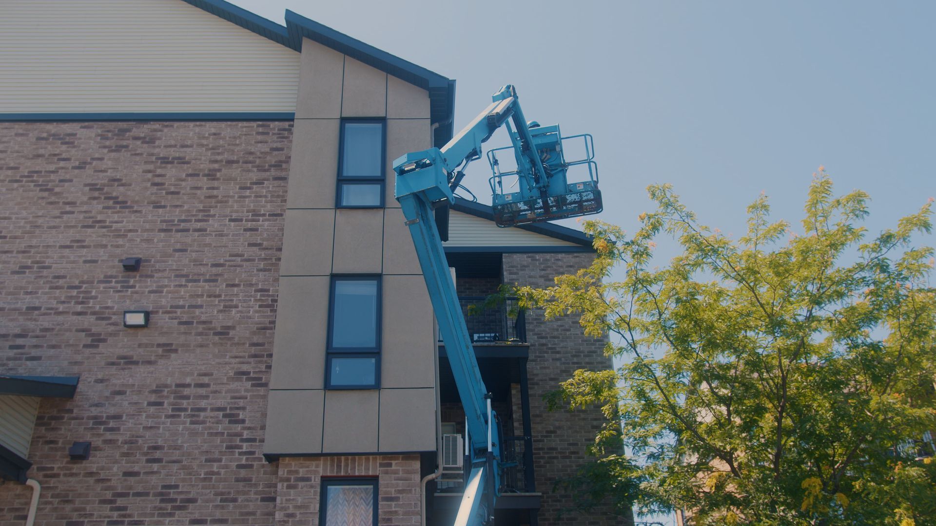 Une plateforme élévatrice bleue près d'un bâtiment en briques. Elle dessert une partie du bâtiment ornée de boiseries.