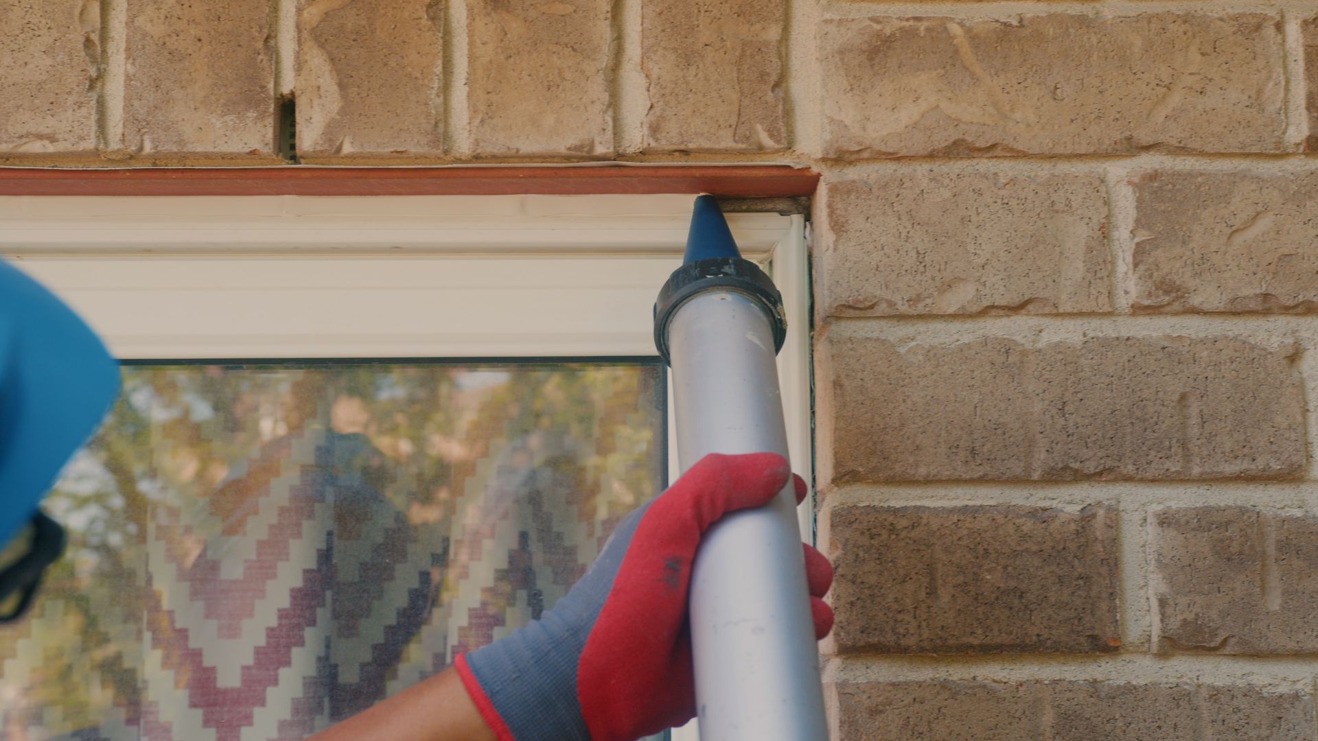 Un homme applique du mastic sur une fenêtre sur un mur de briques.