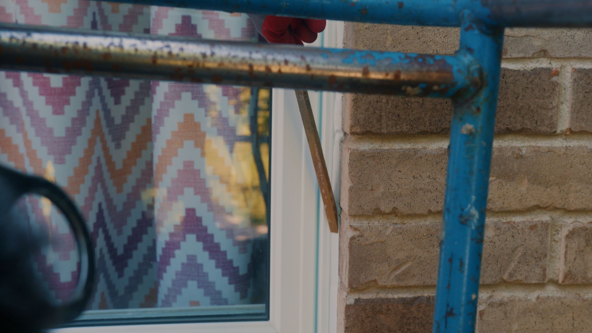 Un serpent se glisse à travers un cadre de fenêtre ouvert, vu partiellement derrière une balustrade bleue.