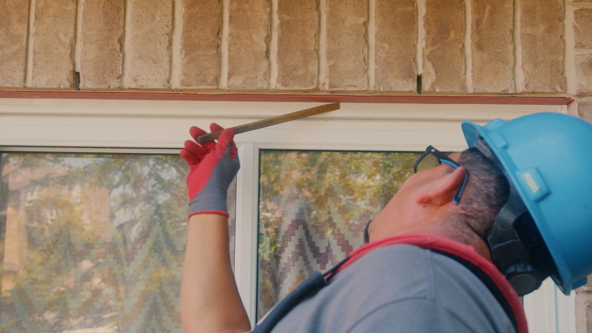 Une personne portant un casque de sécurité mesure au-dessus d'une fenêtre sur un bâtiment en briques.