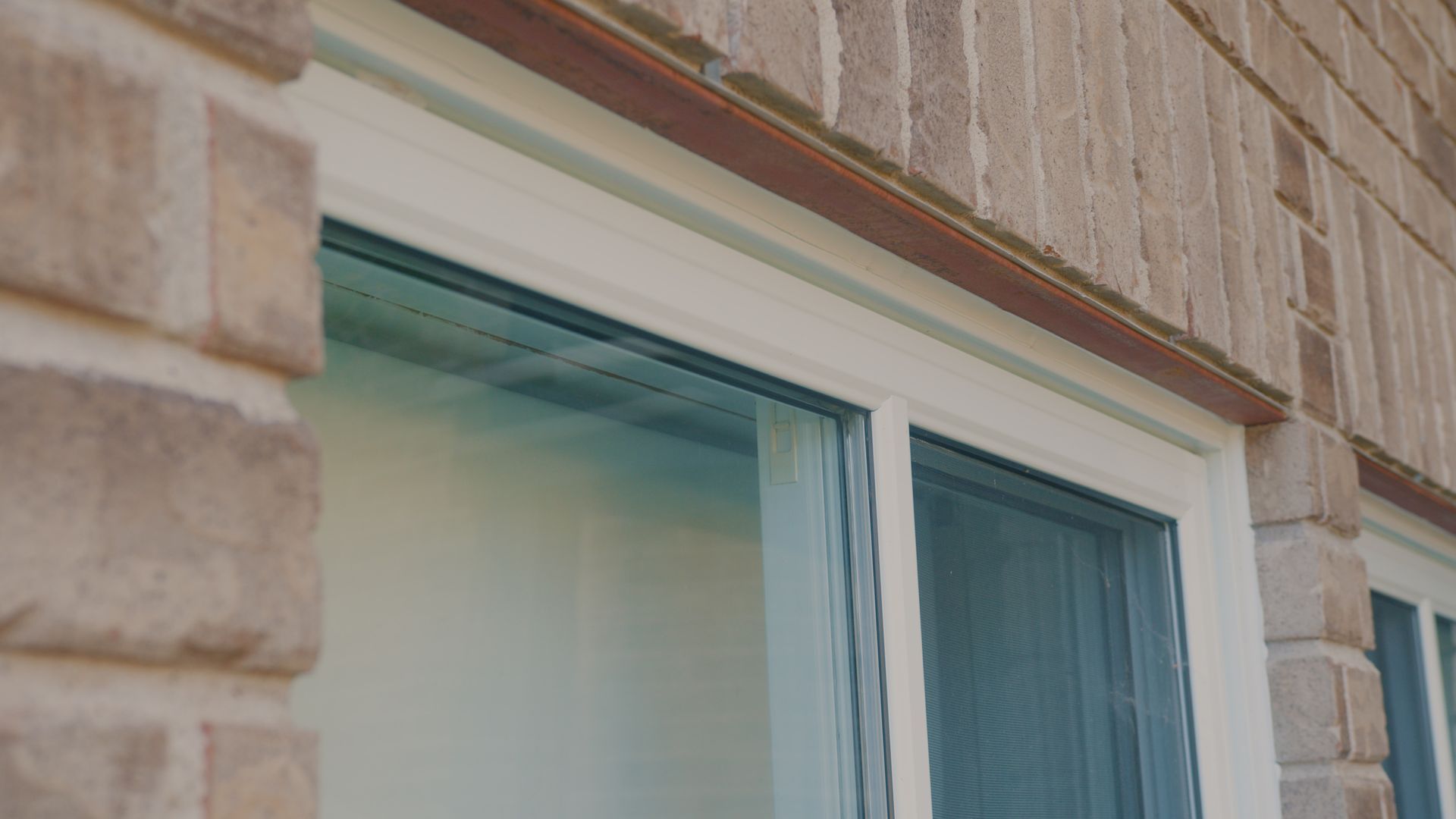 Fenêtre à cadre blanc avec moustiquaire et poutre en bois marron, adossée à un mur de briques.