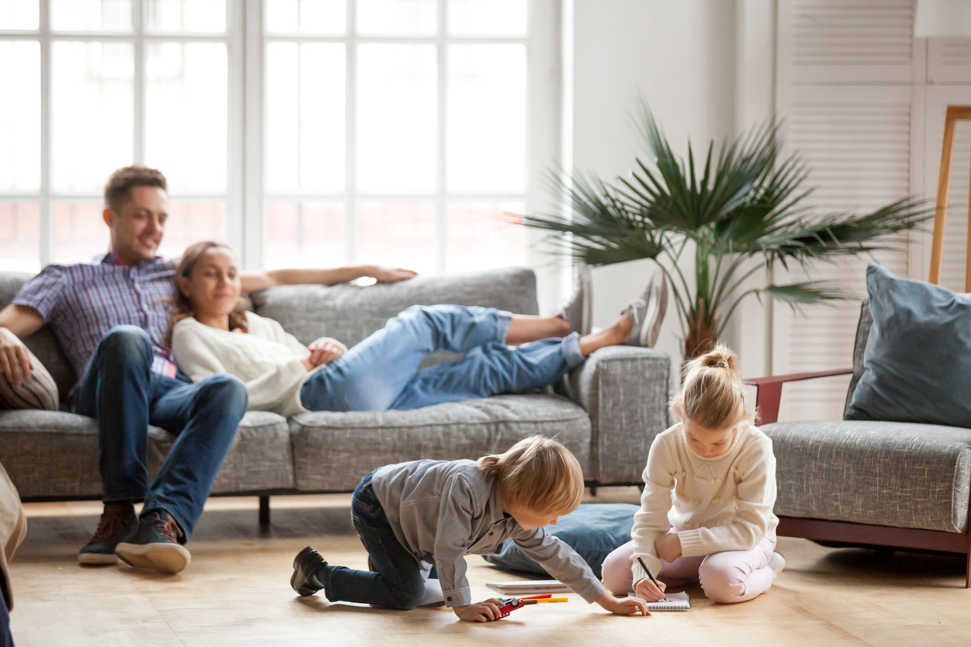 A family is sitting on a couch in a living room while two children are playing on the floor.