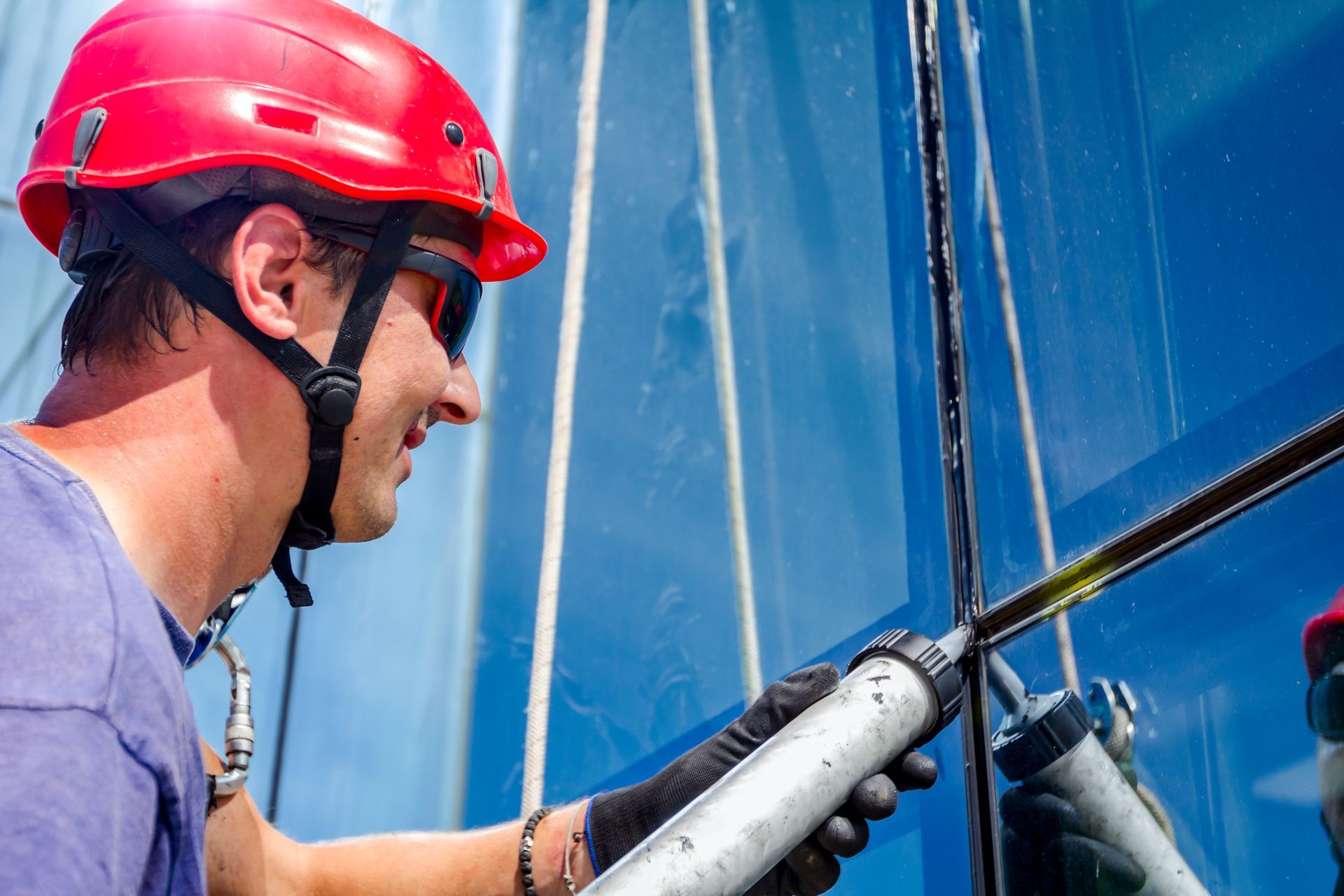 Un homme portant un casque rouge applique du mastic sur une fenêtre.