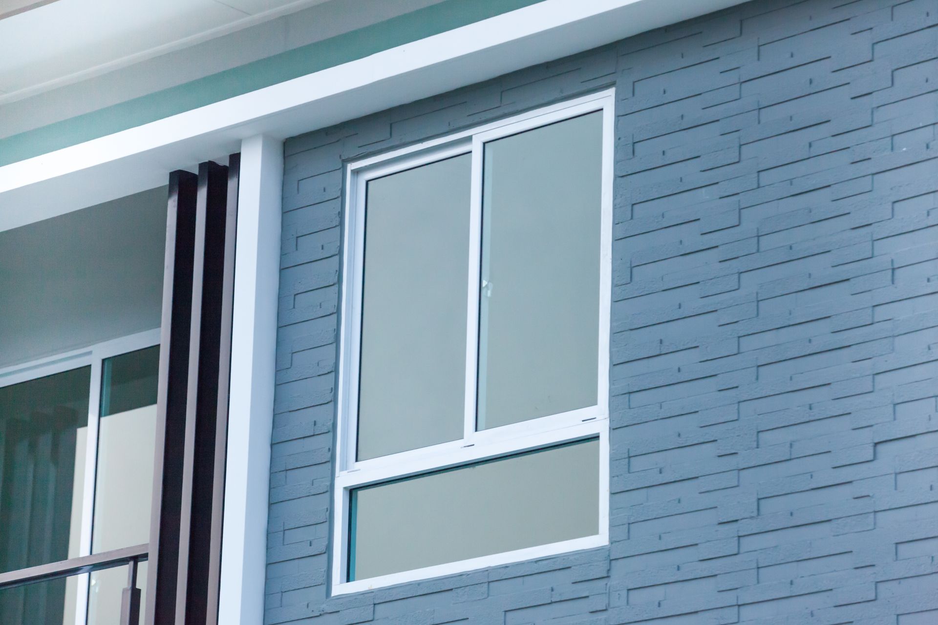 Fenêtre à cadre blanc sur un mur de briques bleues, partiellement ouverte.