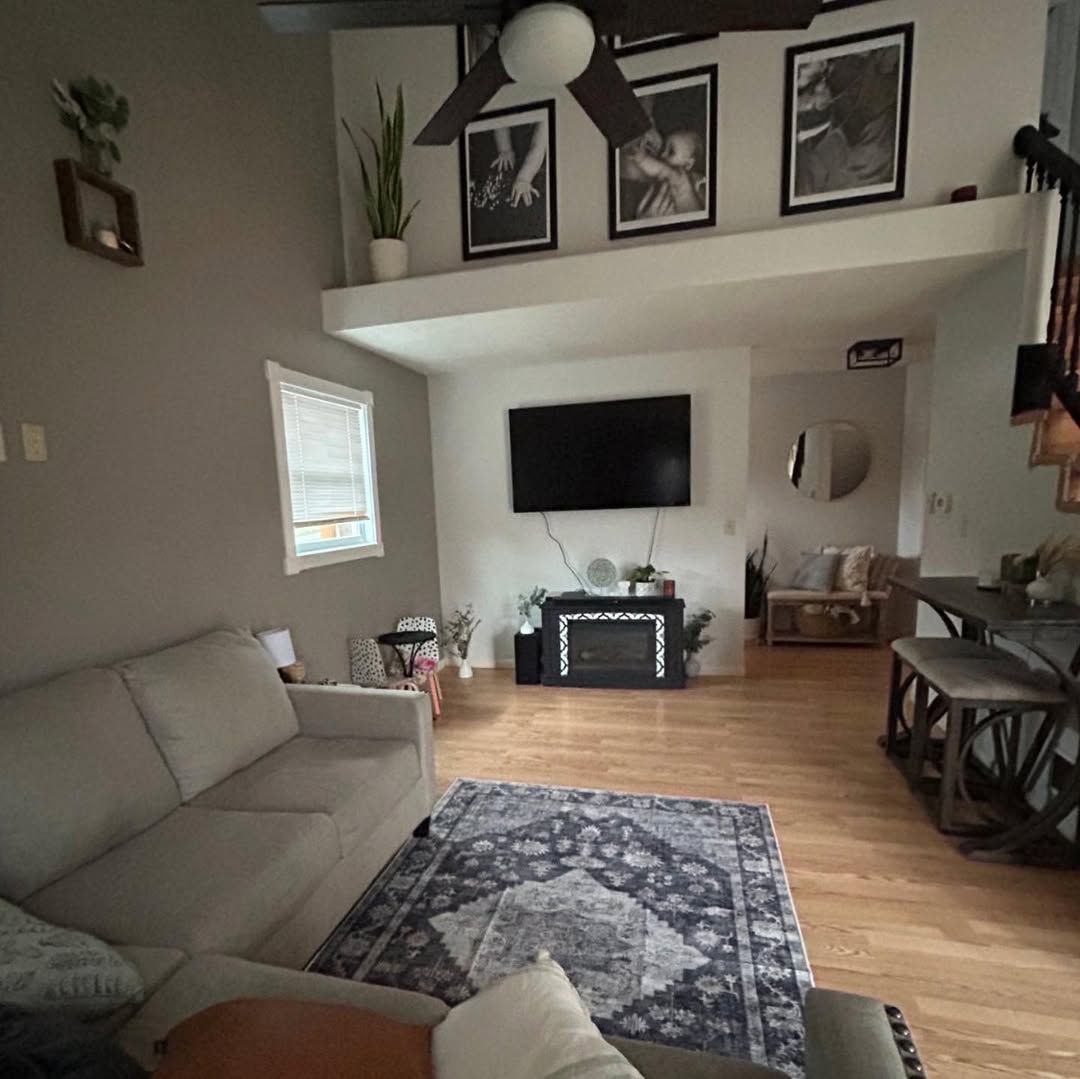 A living room with a couch , rug , television and ceiling fan.