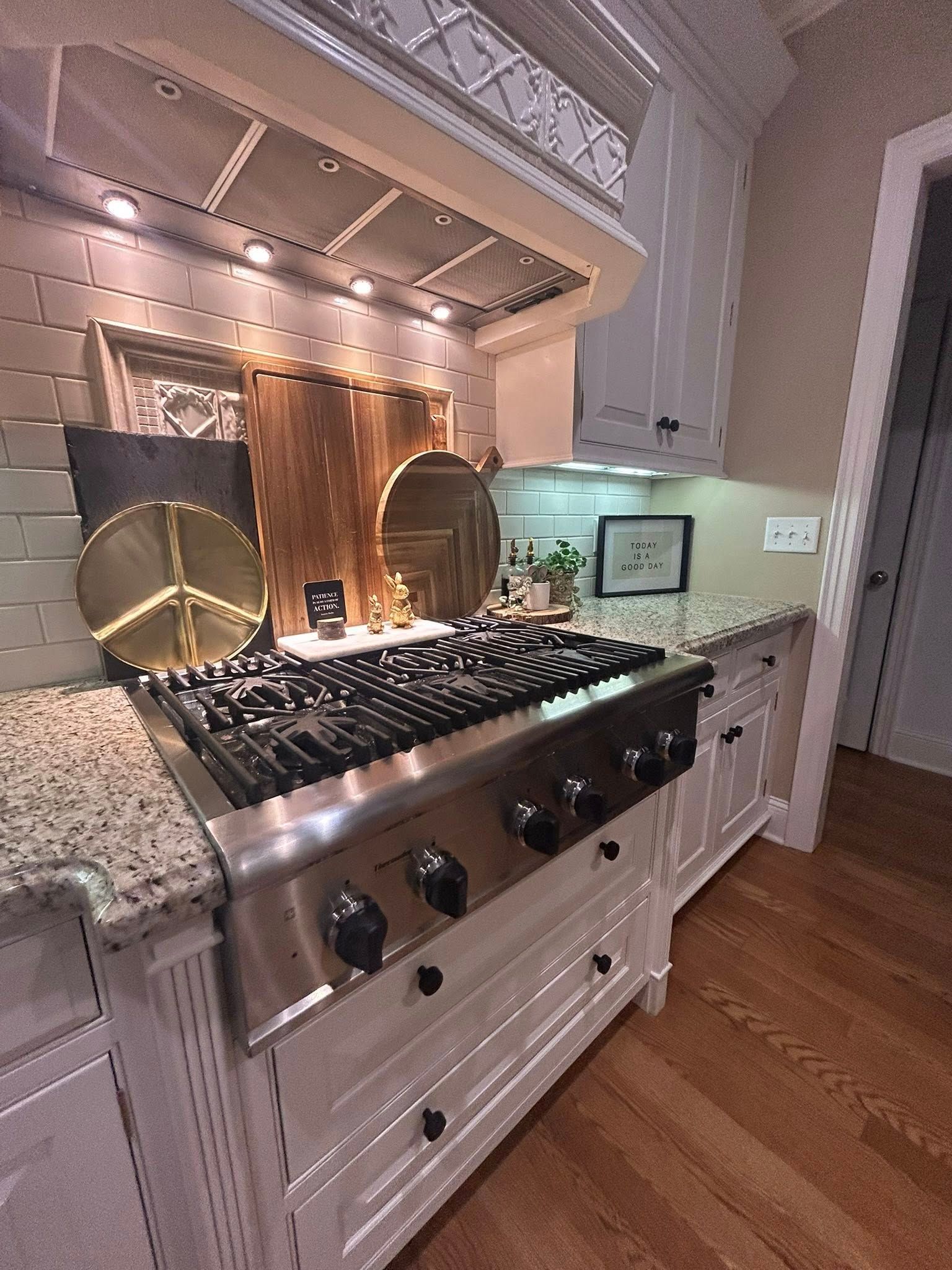 Woman with long blonde hair, smiling, standing in front of blue tile wall and white cabinets.