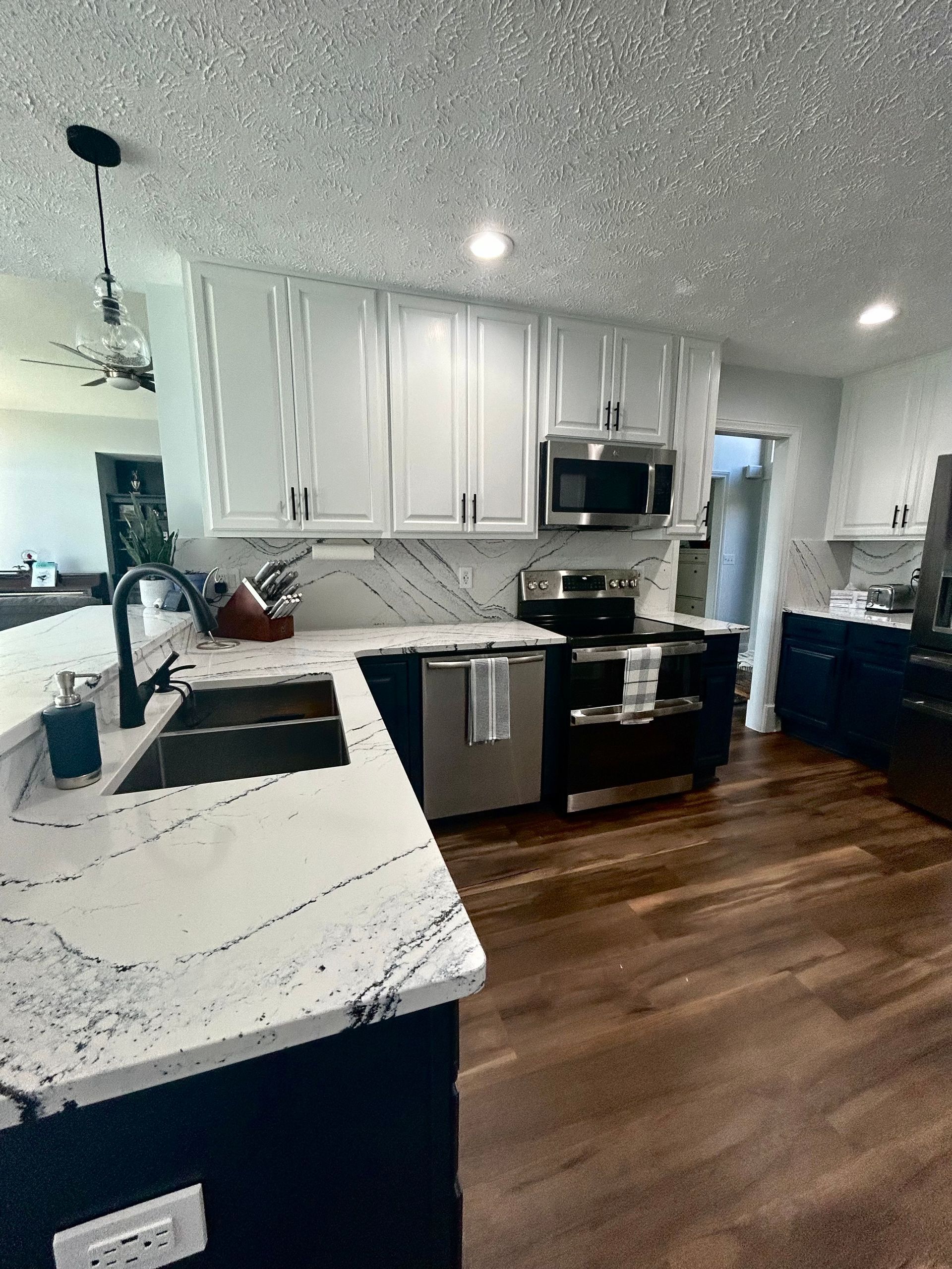 Modern kitchen with white upper cabinets, dark blue base cabinets, and marble countertops.
