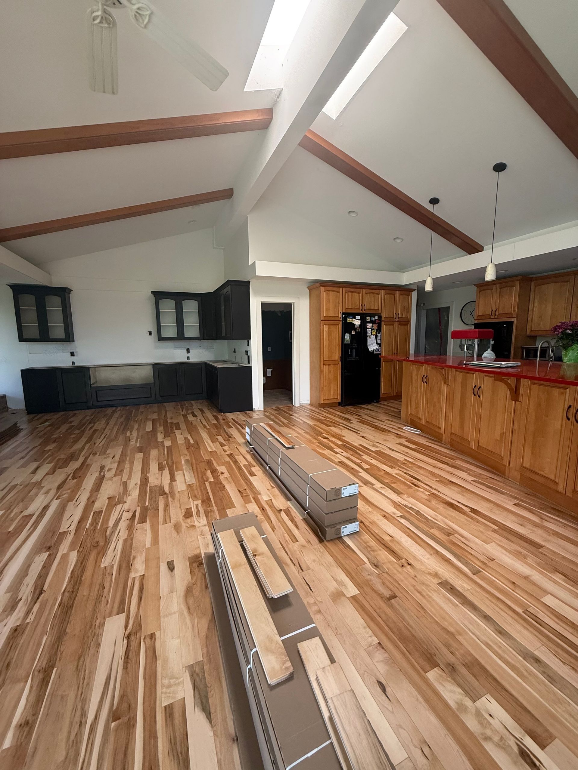 Hardwood flooring being installed in a kitchen. Exposed beams, skylights, dark cabinets, and wood countertops.