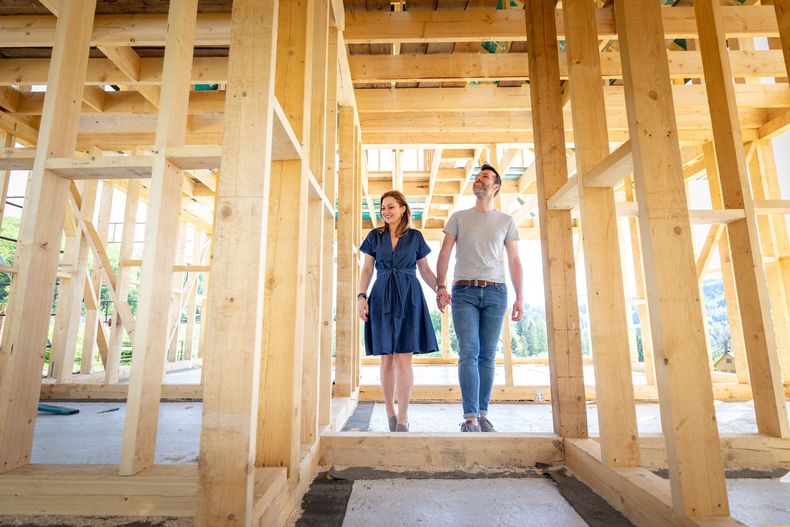 A man and a woman are holding hands in a wooden house under construction.
