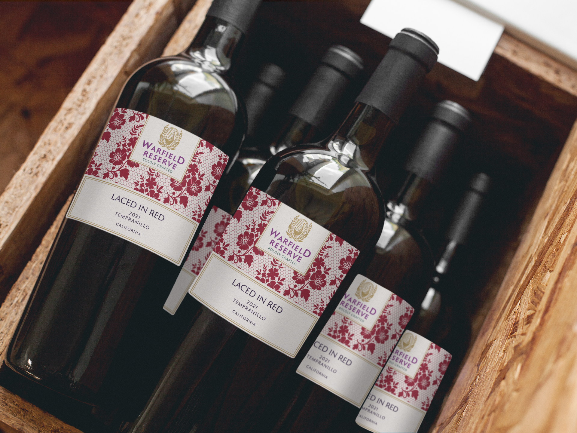 Wooden crate filled with bottles of red wine, with white labels and floral designs.
