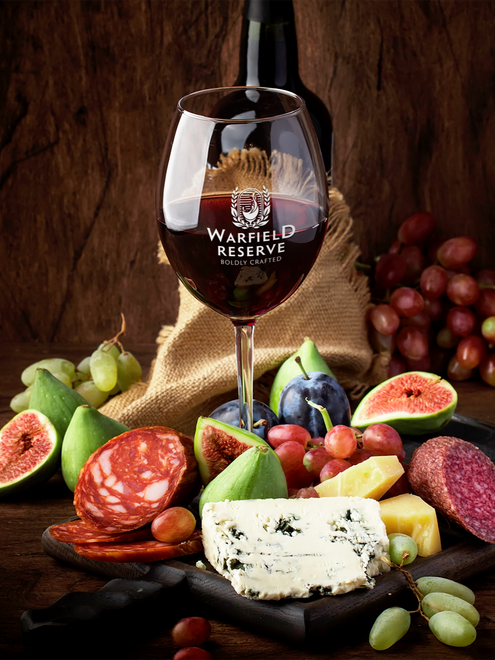 A wine glass filled with red wine, charcuterie board with cheese, grapes, figs, salami, and a wine bottle.