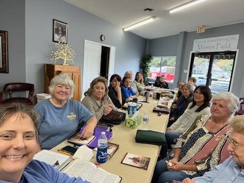 Group of people seated at a long table in a room; some smiling at the camera.