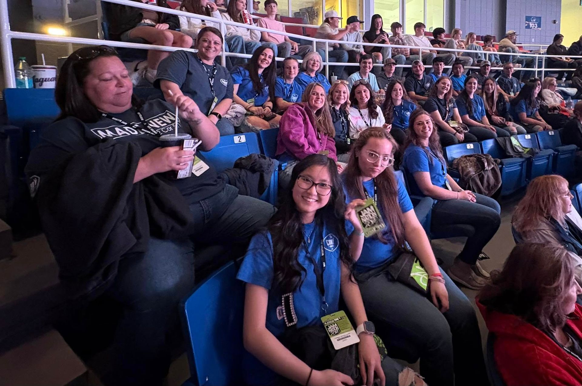 People in blue shirts seated in an auditorium, smiling at the camera.