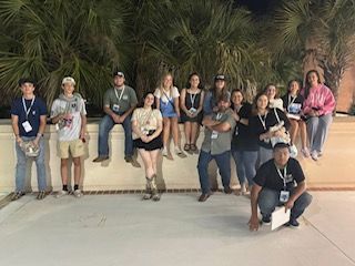 People in blue shirts seated in an auditorium, smiling at the camera.