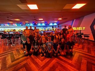 Six people looking up, seated on a bench, near a table with food.