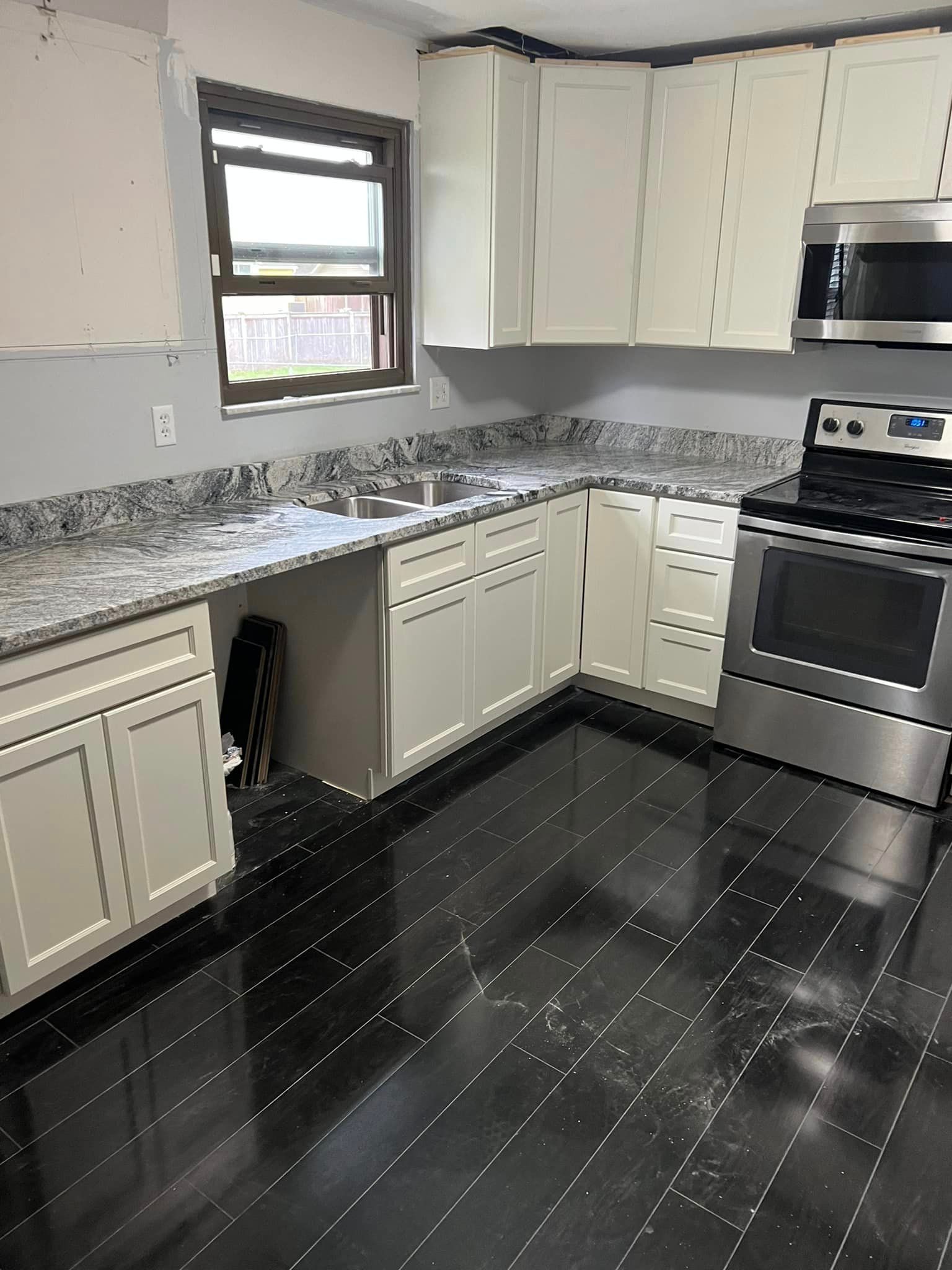 A kitchen with white cabinets , stainless steel appliances , a sink , and a window.