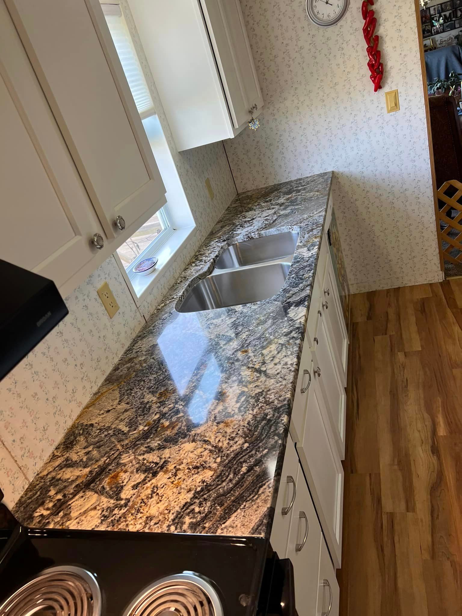 A kitchen with a granite counter top , stove , sink and cabinets.