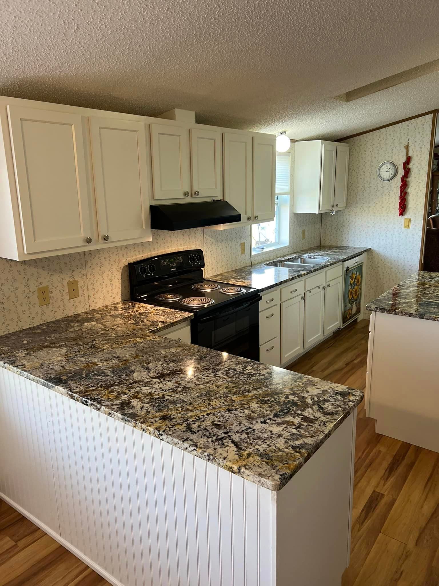 A kitchen with granite counter tops , white cabinets and a stove.