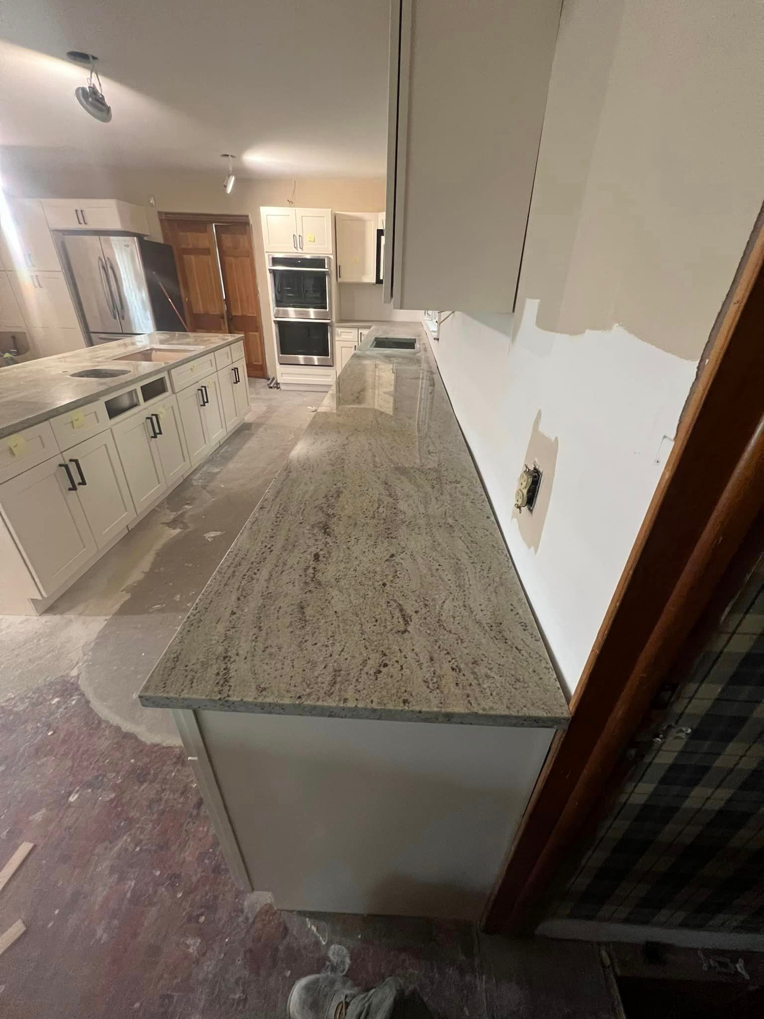 A kitchen under construction with white cabinets and granite counter tops.