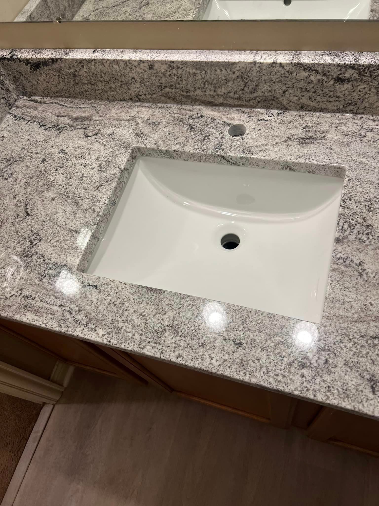 A bathroom sink with a granite counter top and a mirror.