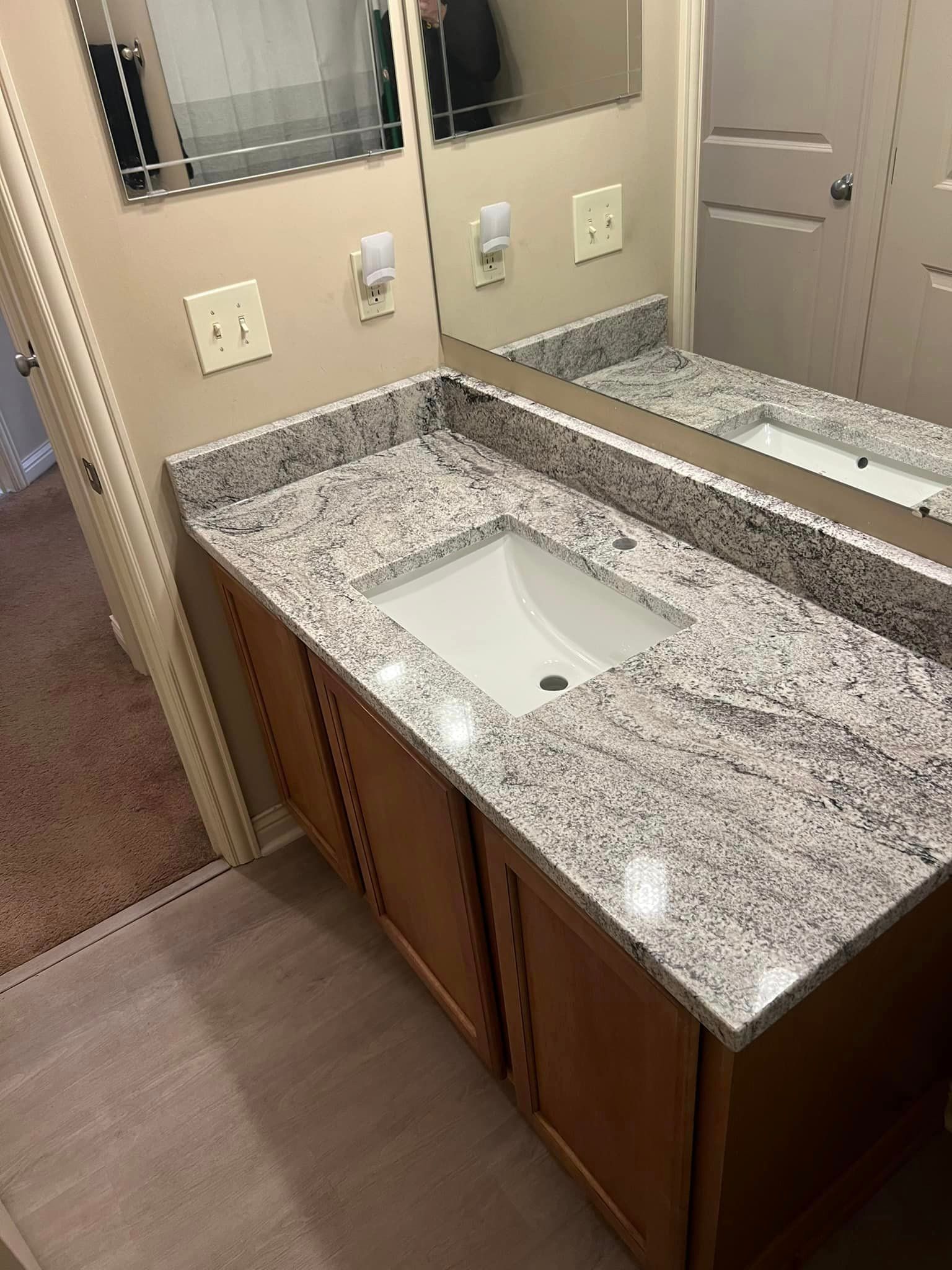 A bathroom with a sink , mirror and granite counter top.