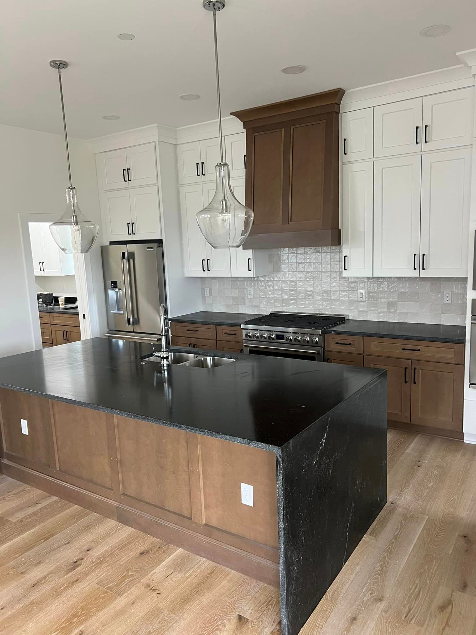 A kitchen with wooden cabinets , black counter tops , stainless steel appliances and a large island.