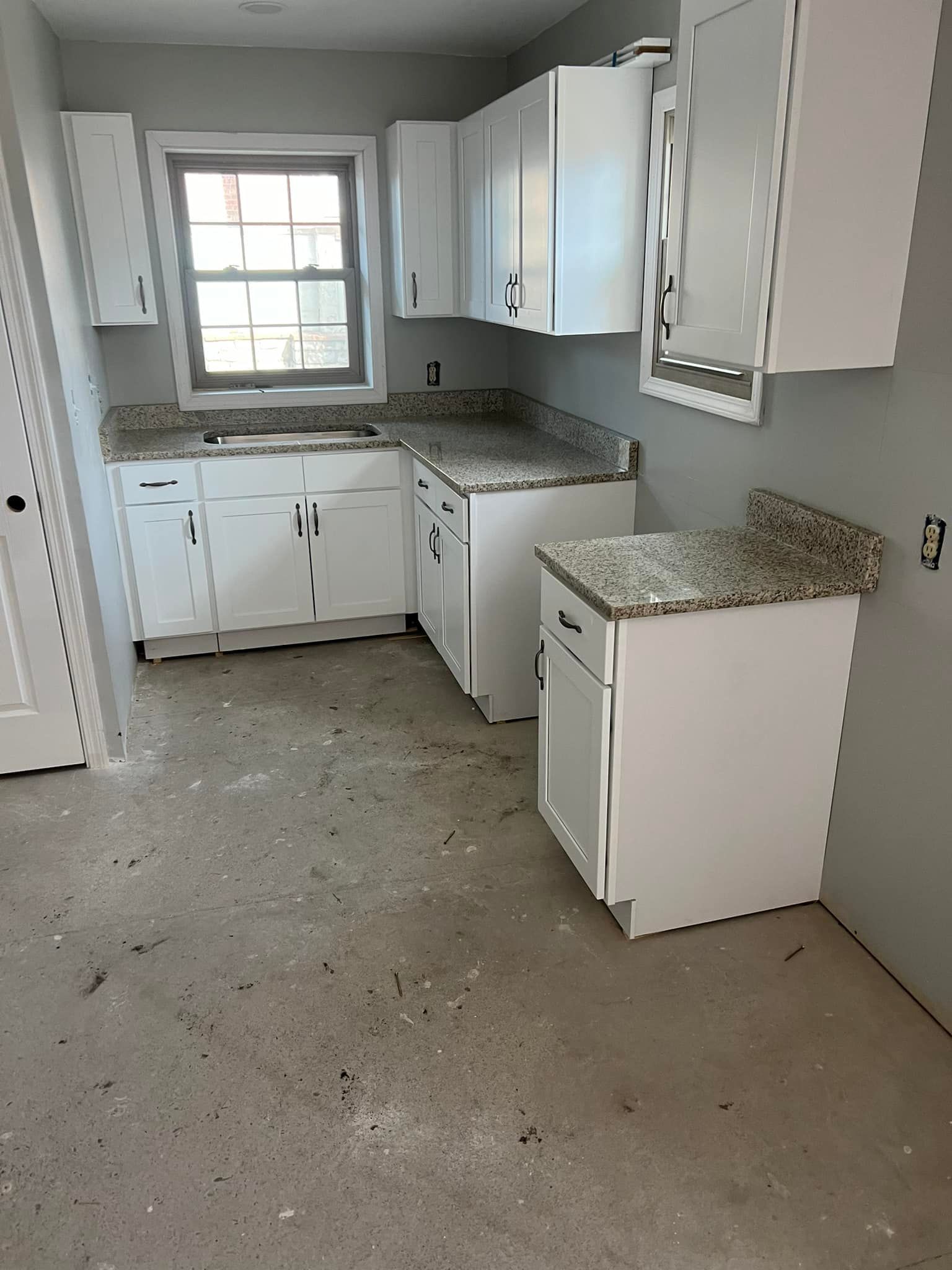 An empty kitchen with white cabinets and granite counter tops.