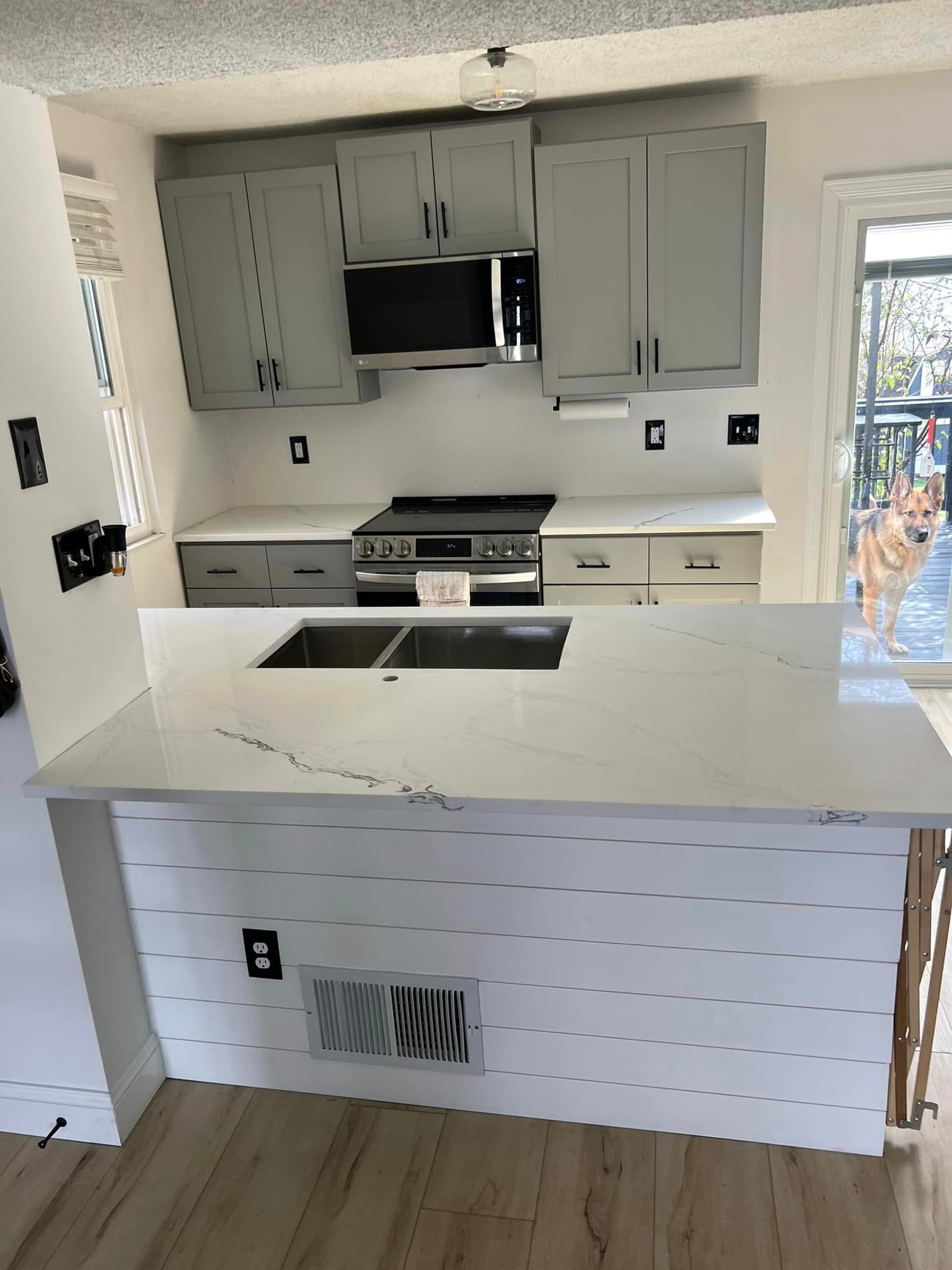 A kitchen with gray cabinets , white counter tops , a stove and a sink.