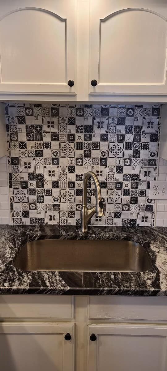 A kitchen sink with a checkered tile backsplash and a faucet.