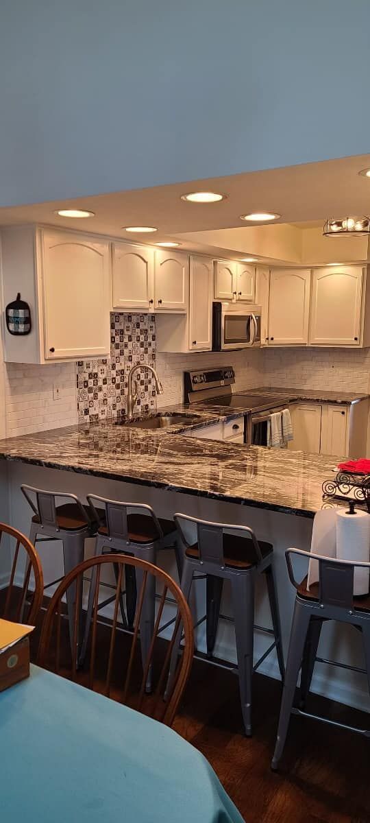 A kitchen with white cabinets , granite counter tops , stools and a table.