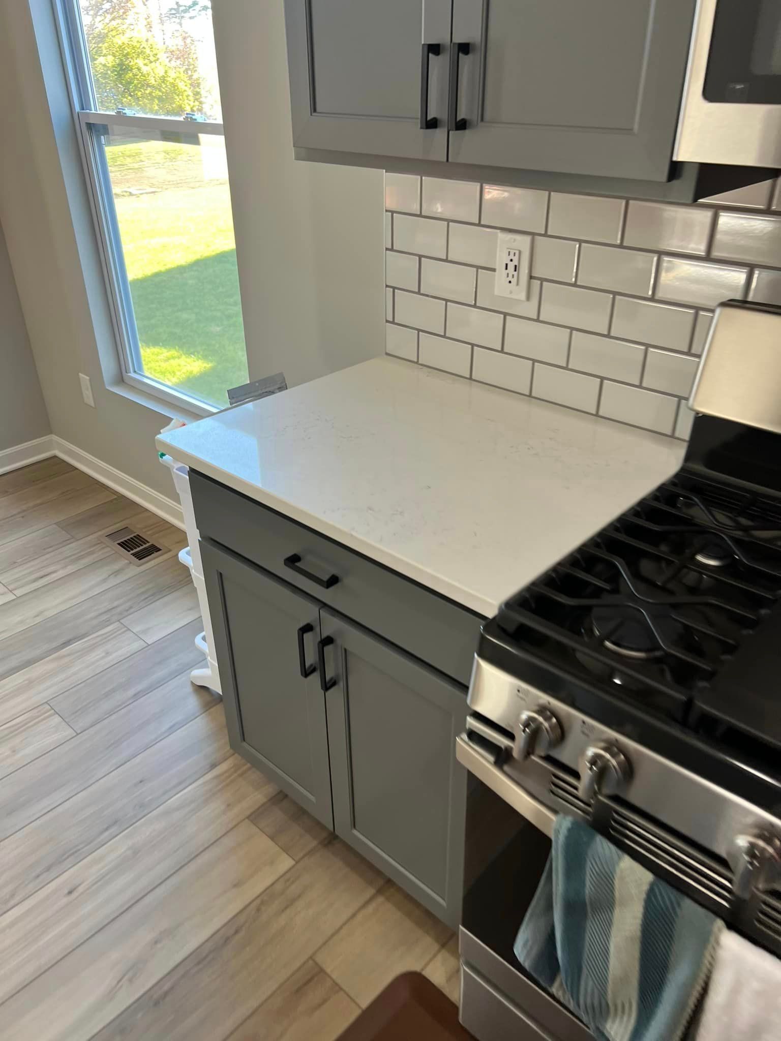 A kitchen with gray cabinets , a stove , a microwave , and a window.