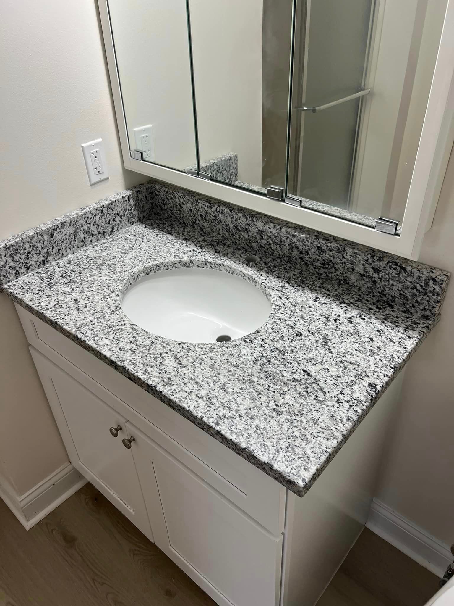 A bathroom sink with a granite counter top and a mirror.