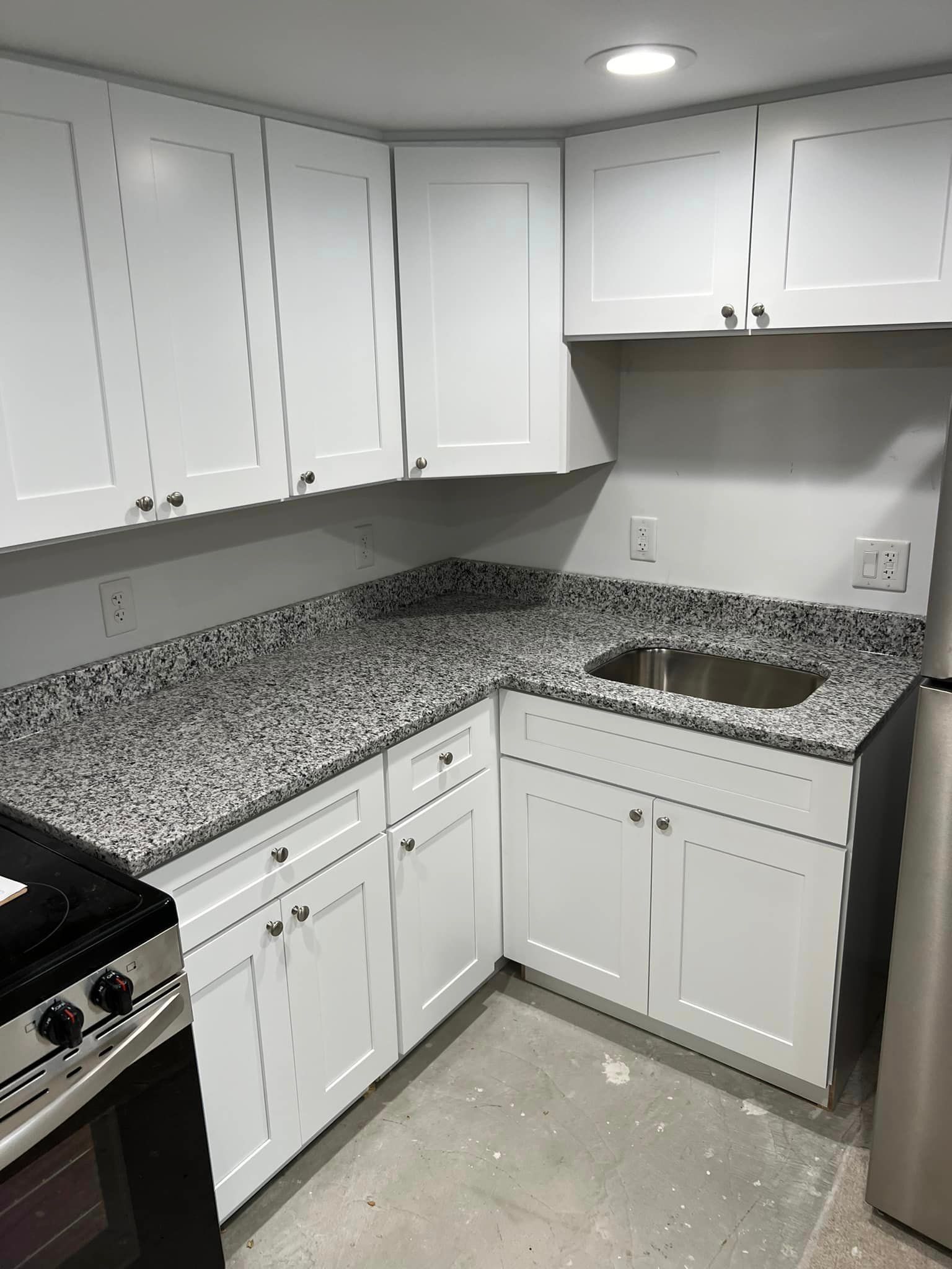 A kitchen with granite counter tops , white cabinets , a stove and a refrigerator.