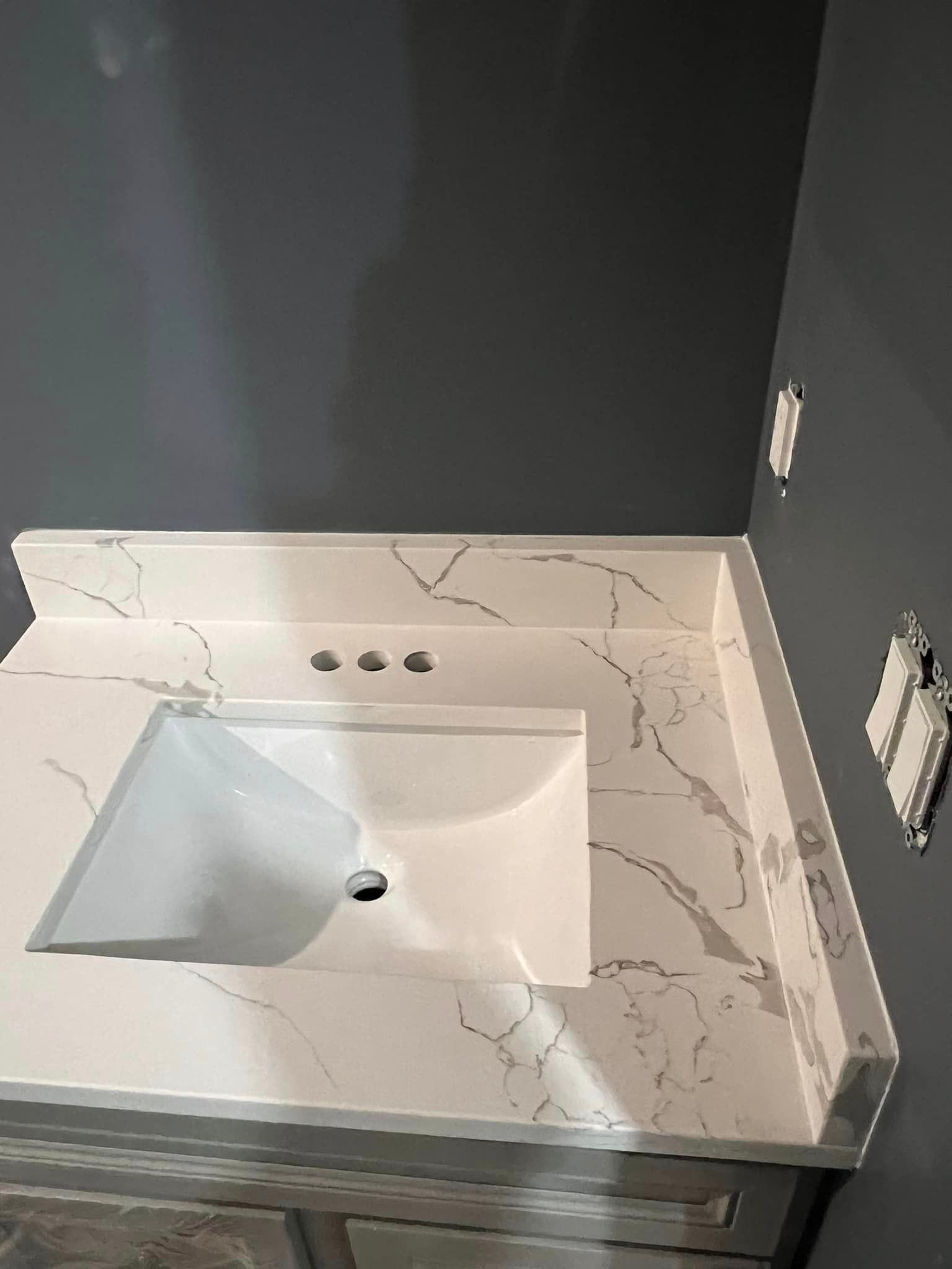 A bathroom sink with a marble counter top and a gray wall.