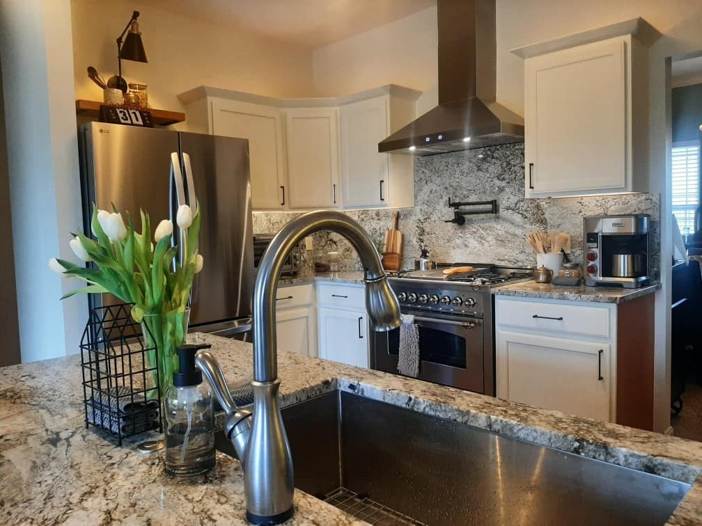 A kitchen with a sink , stove , refrigerator and a vase of flowers on the counter.