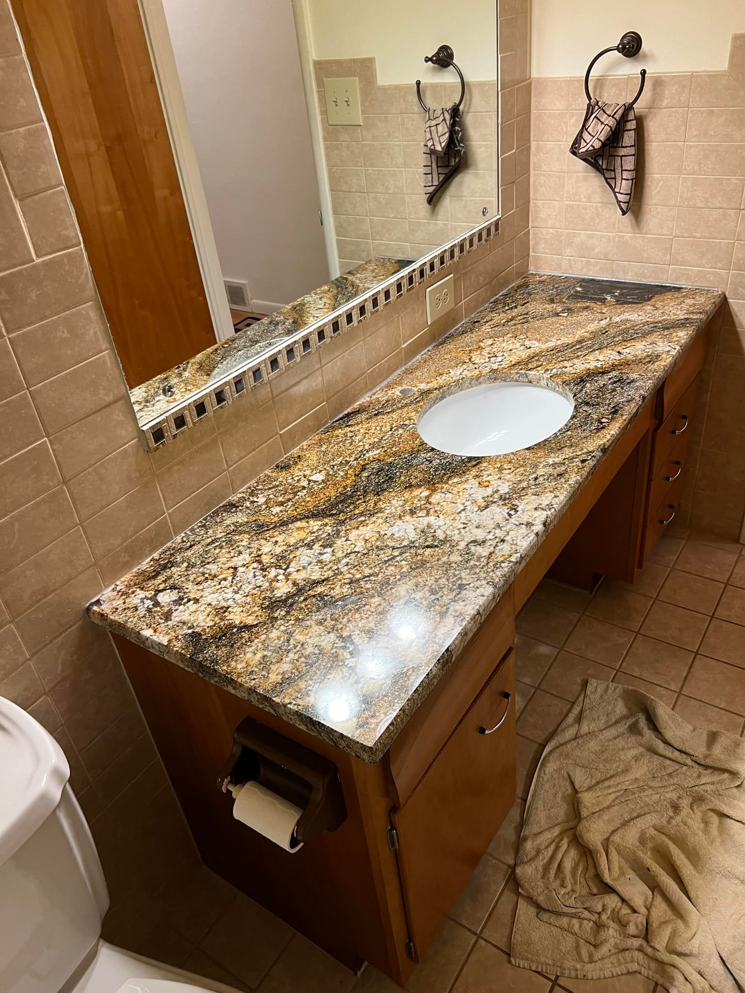 A bathroom with a sink , toilet , mirror and granite counter top.