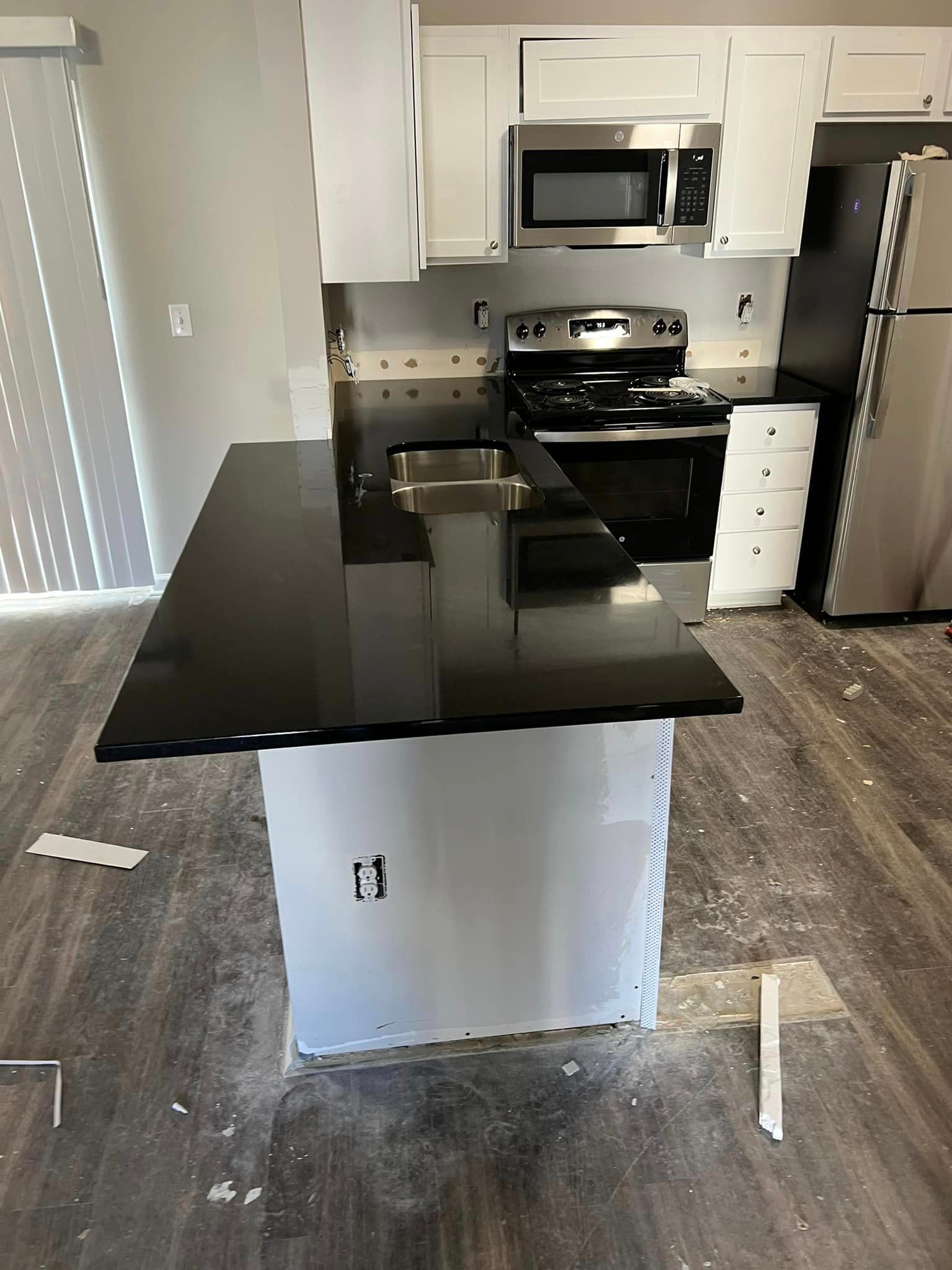 A kitchen with a black counter top , stainless steel appliances , and white cabinets.