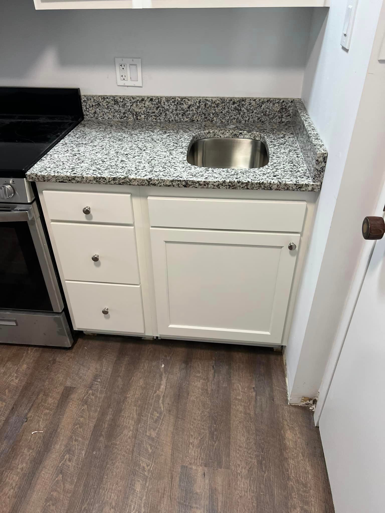 A kitchen with granite counter tops , white cabinets , a stove and a sink.