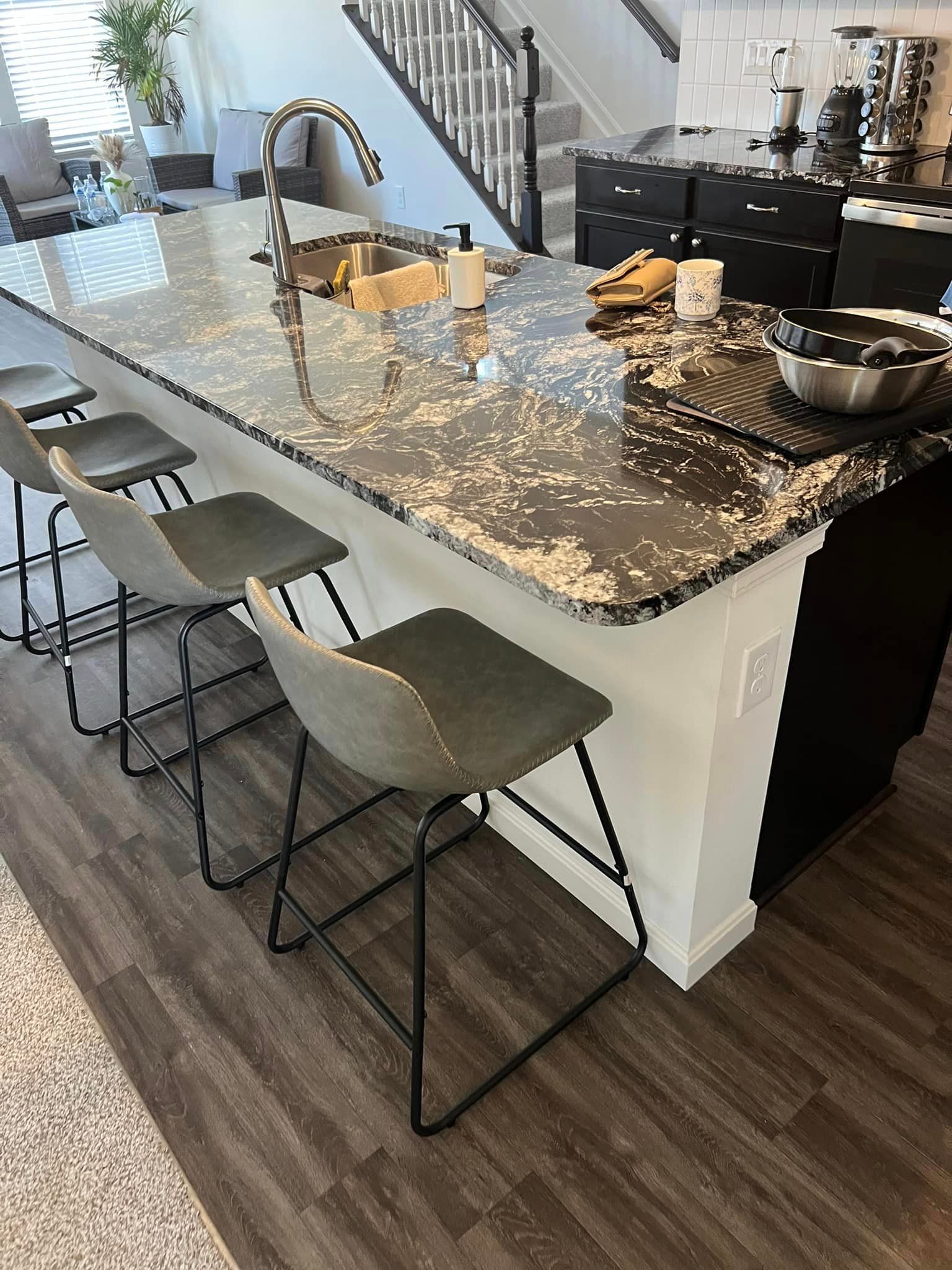 A kitchen with a large island and stools and a sink.