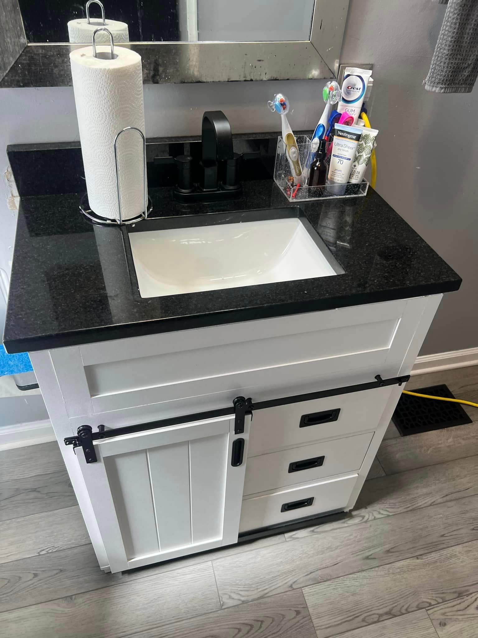 A bathroom vanity with a black counter top and a sink.