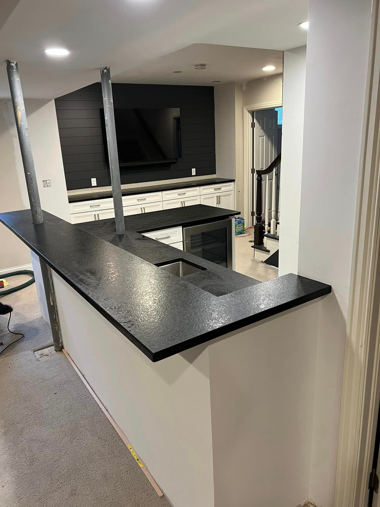 A kitchen with a black counter top and a television on the wall.