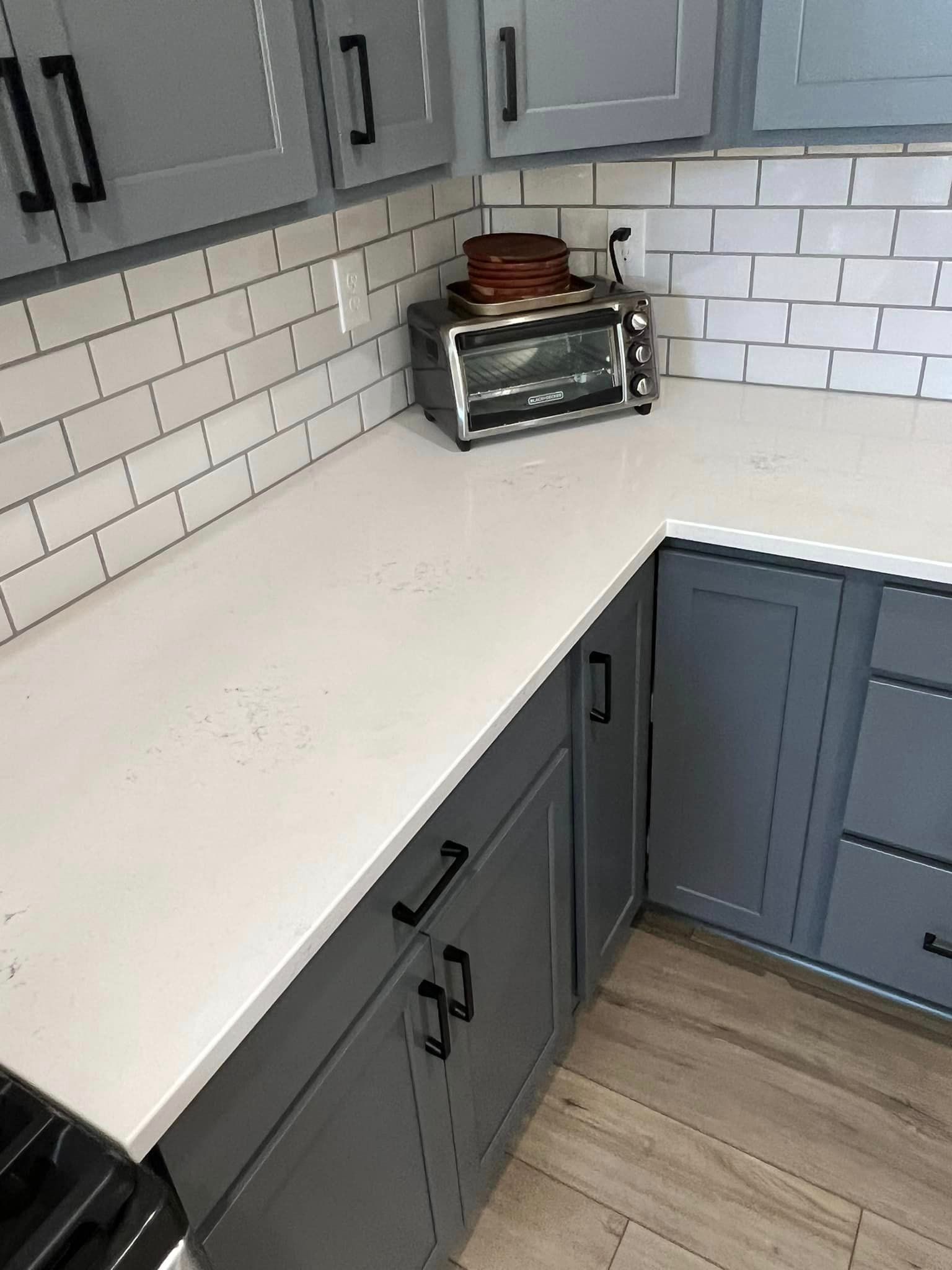 A kitchen with gray cabinets , white counter tops , and a toaster oven.