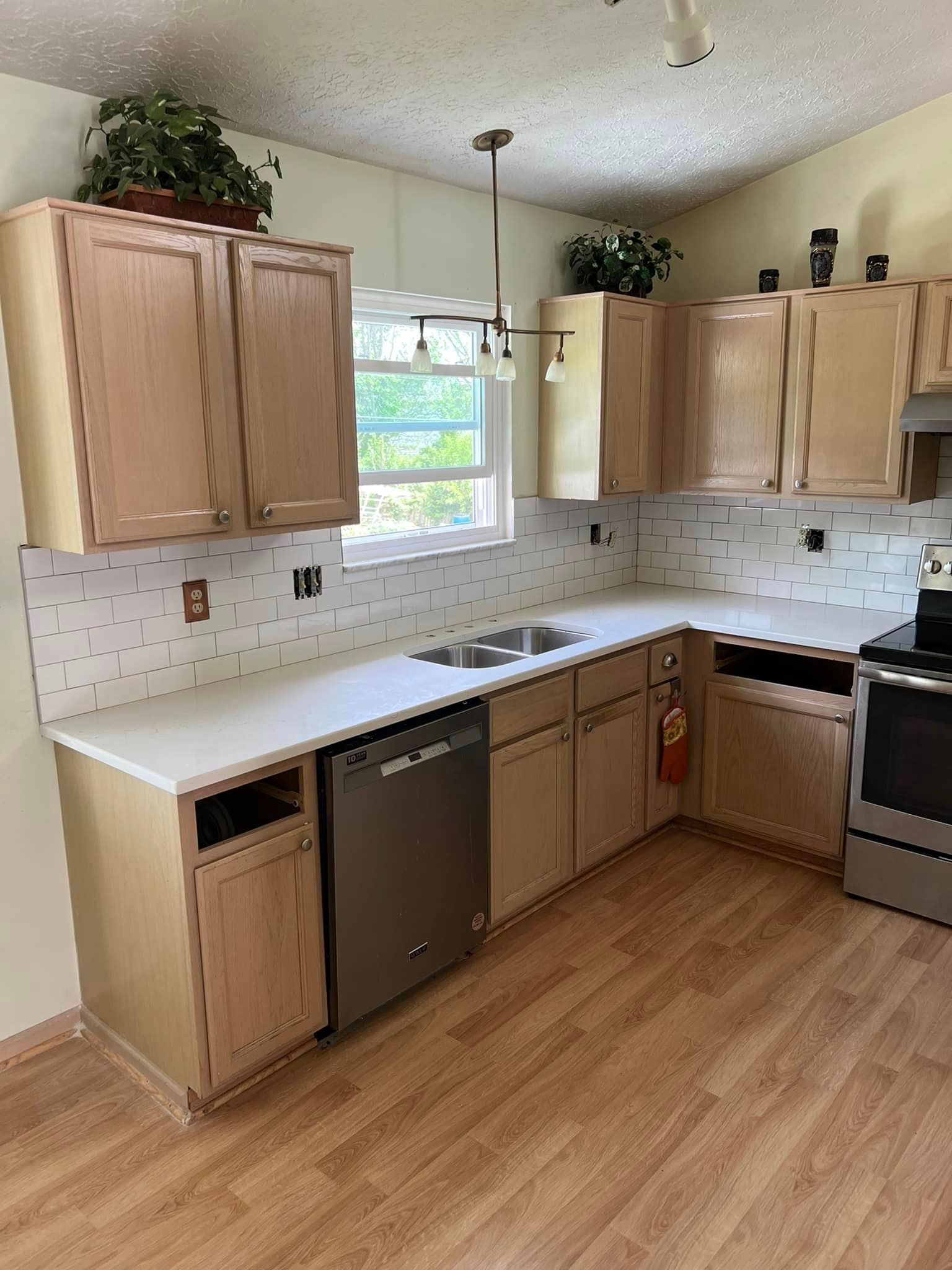 A kitchen with wooden cabinets , a stove , a sink , and a dishwasher.