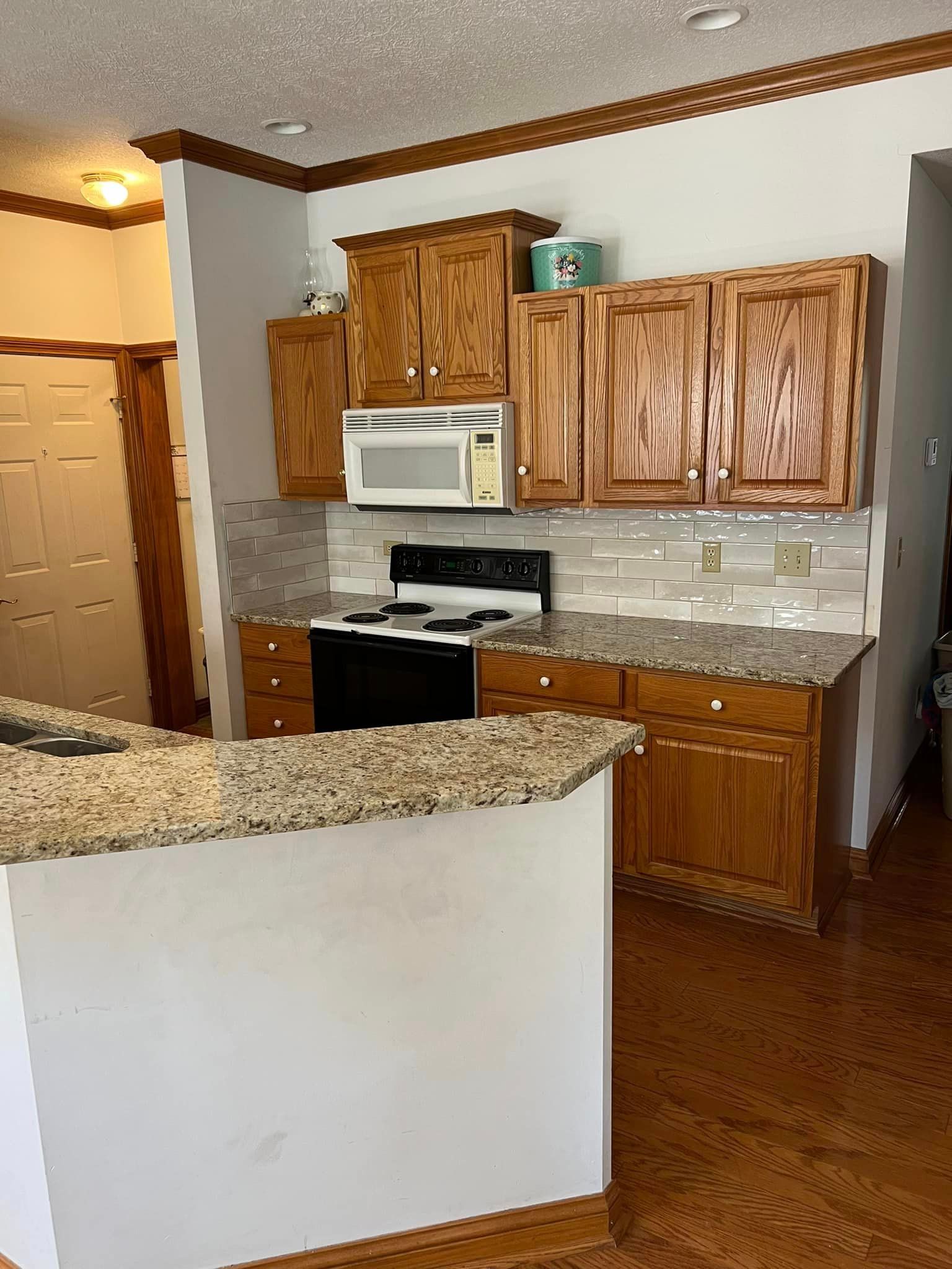A kitchen with wooden cabinets , granite counter tops , a stove and microwave.
